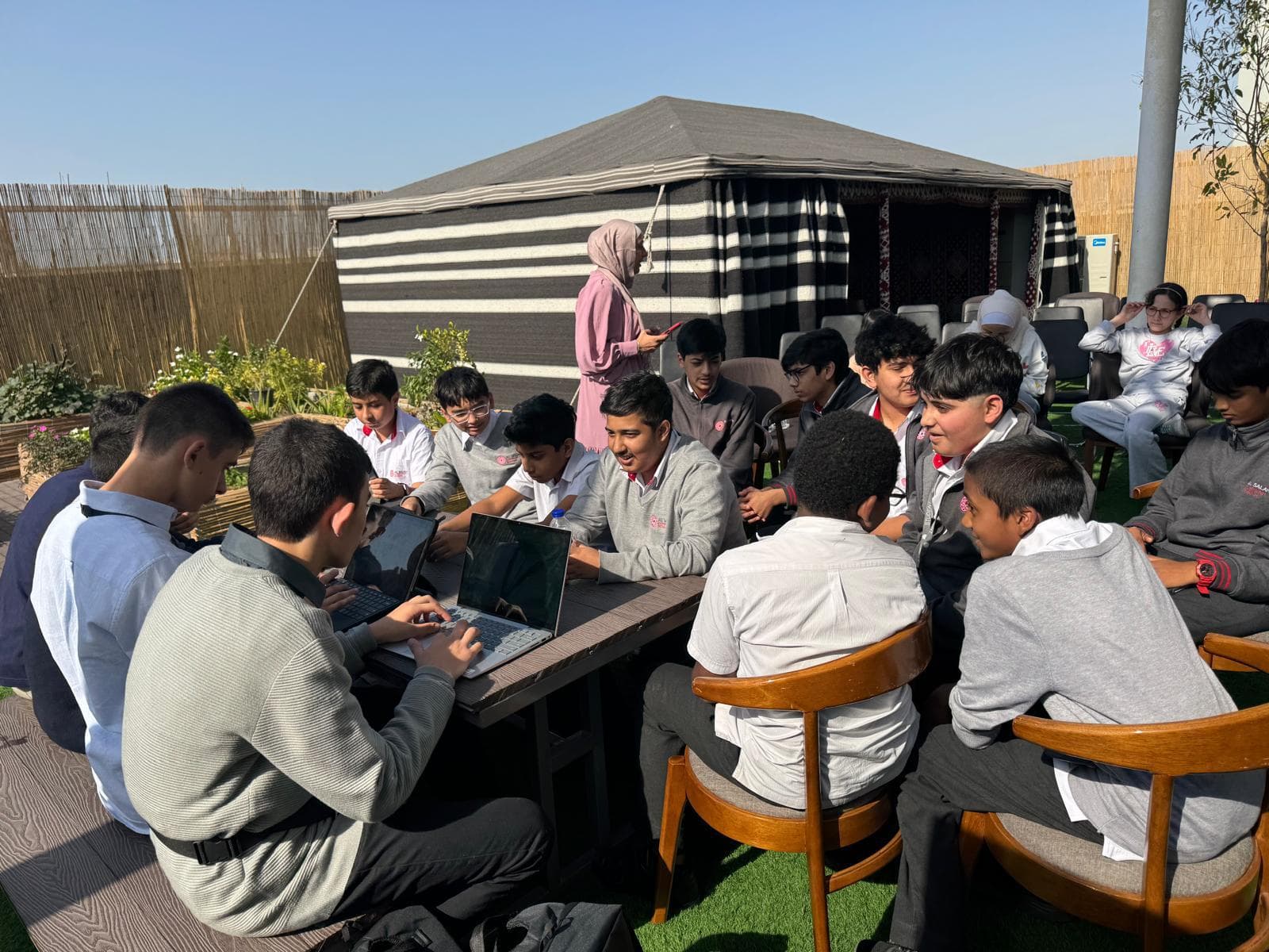 Students working on laptops around an outdoor table with students from a local school